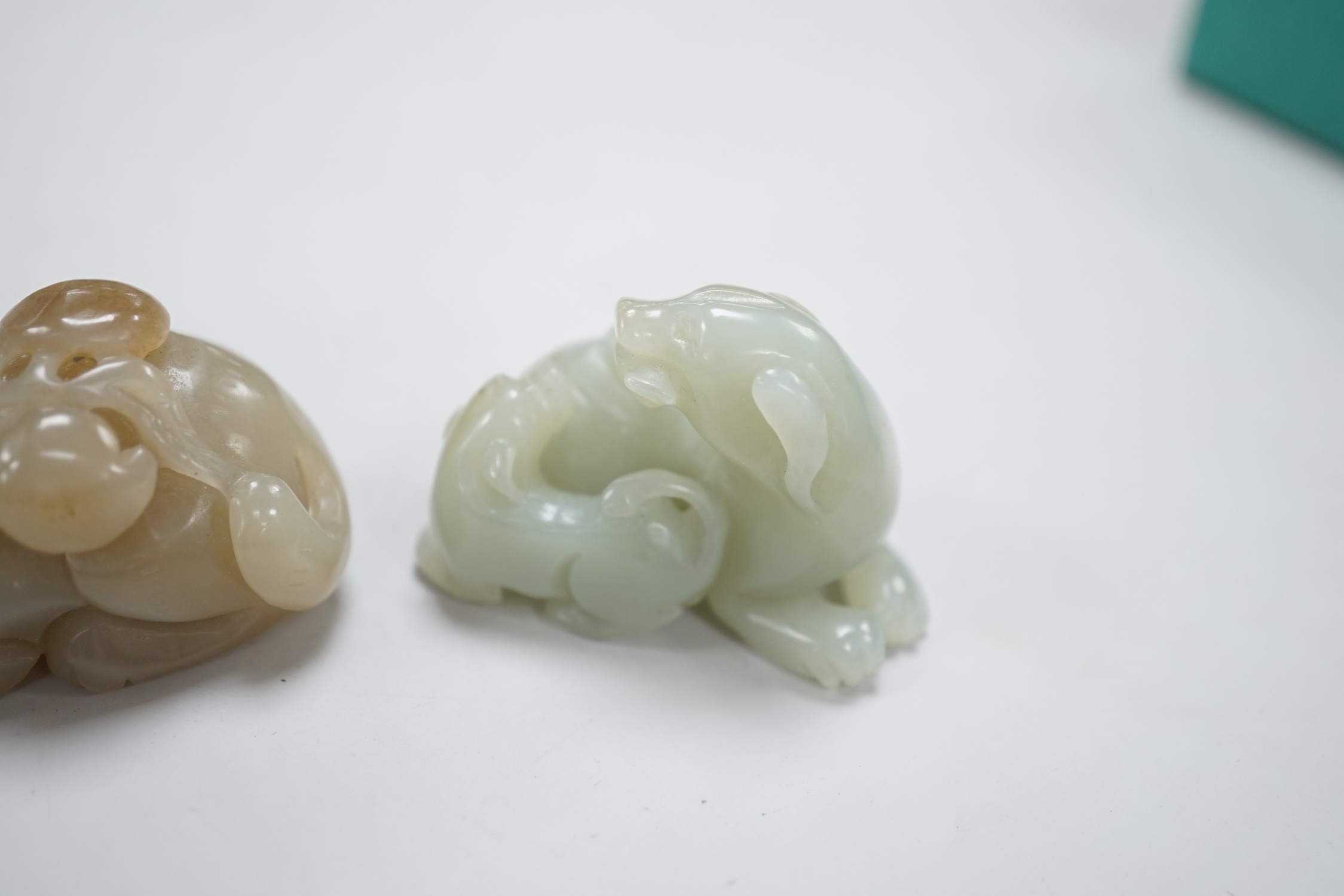 A Chinese celadon and brown jade figure of a cat biting a peach branch and a celadon jade group of a dog and puppy, cat biting a peach branch 5cm wide (2)